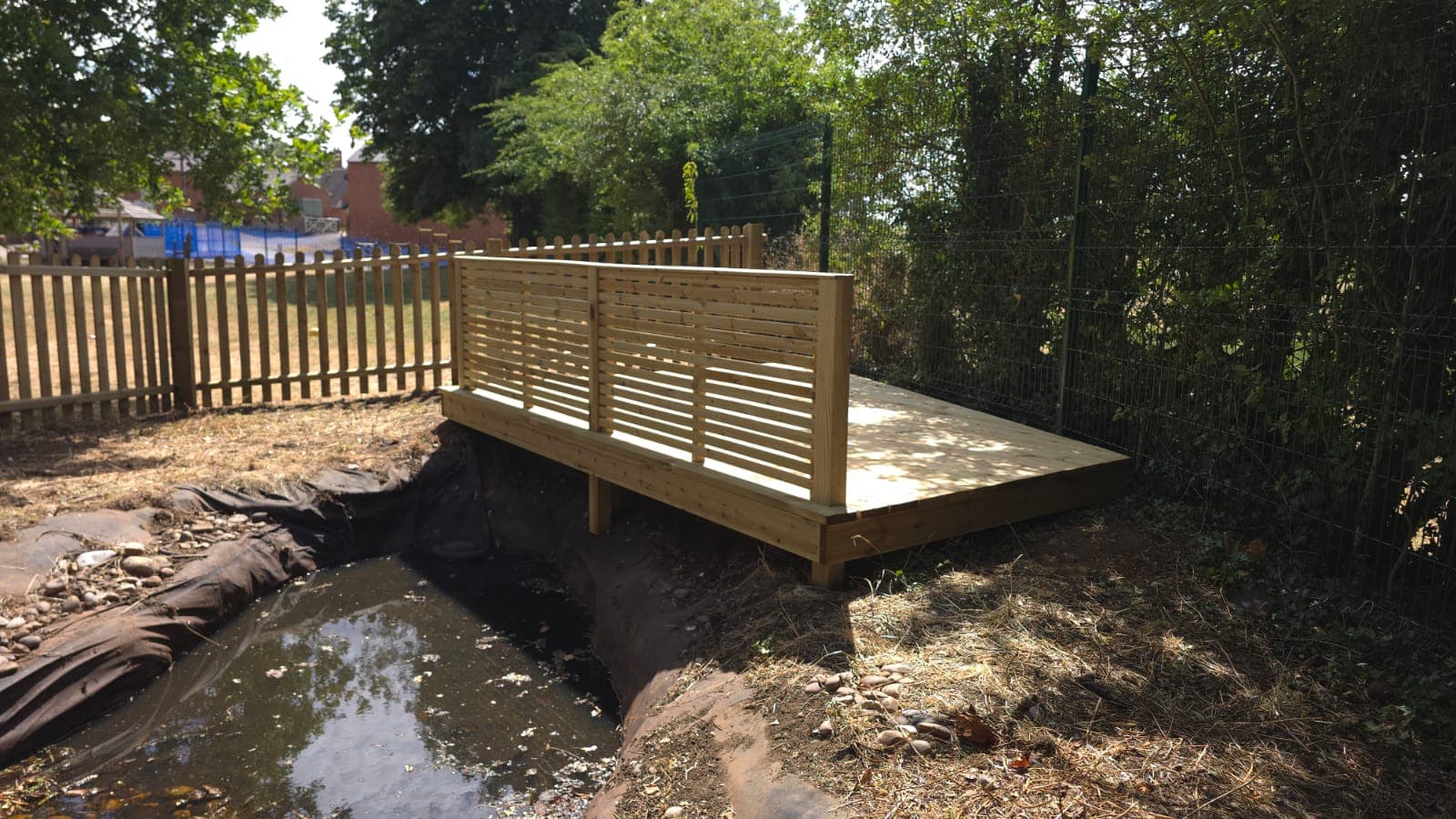 New raised timber decking spanning the school pond with a horizontal slatted balustrade